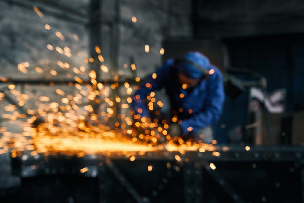 Close up of young man in blue special uniform doing gate by electric steel cutter machine for welding special metal. Concept of process produce modern fence in garage.